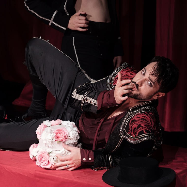 Luka Jozic reclining in red and black costume, holding a bouquet